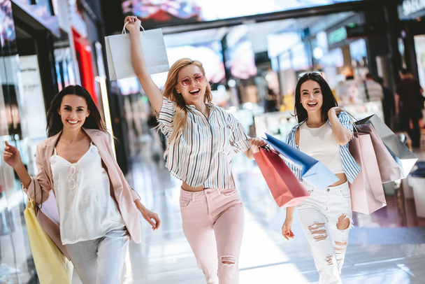 Three attractive young girls are doing shopping with shopping bags in modern mall. - Foto, imagen