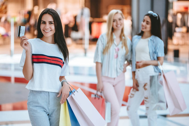 Three attractive young girls are doing shopping with shopping bags in modern mall. - Photo, Image