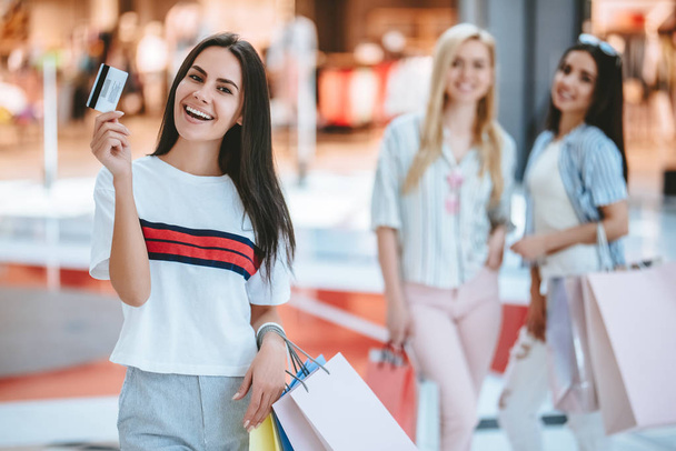Three attractive young girls are doing shopping with shopping bags in modern mall. - Zdjęcie, obraz