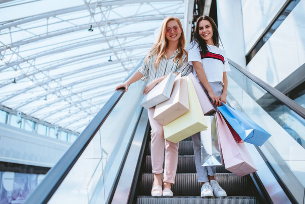 Two attractive young girls are doing shopping with shopping bags in modern mall. - Valokuva, kuva