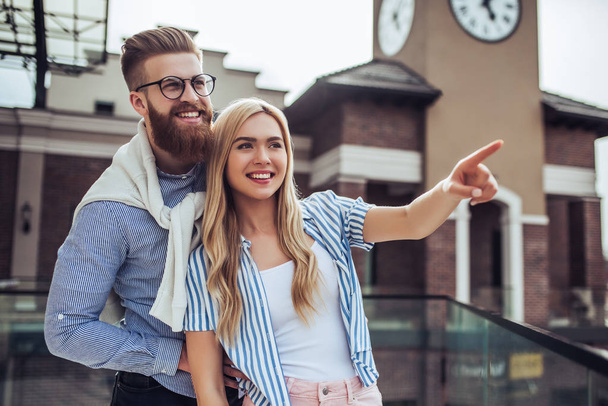 Young stylish happy couple is spending time together outdoors. Attractive woman and handsome bearded man are having fun together in the city. - Фото, изображение