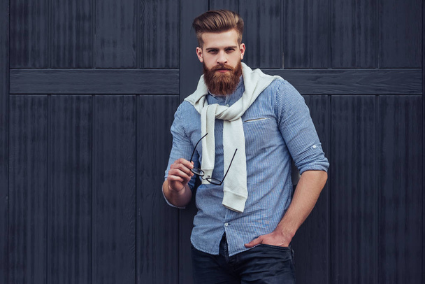 Stylish bearded man is posing on black wooden background in the city. Young man with eye glasses isolated. - Foto, afbeelding