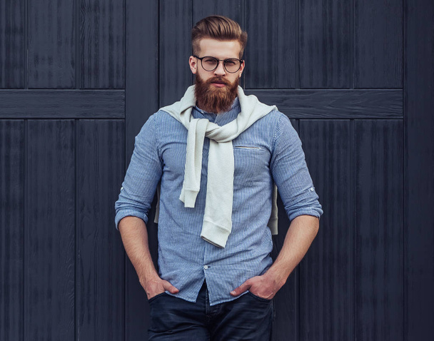 Stylish bearded man is posing on black wooden background in the city. Young man in eye glasses isolated. - Photo, Image