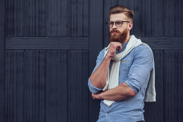 Stylish bearded man is posing on black wooden background in the city. Young man in eye glasses isolated. - Photo, Image
