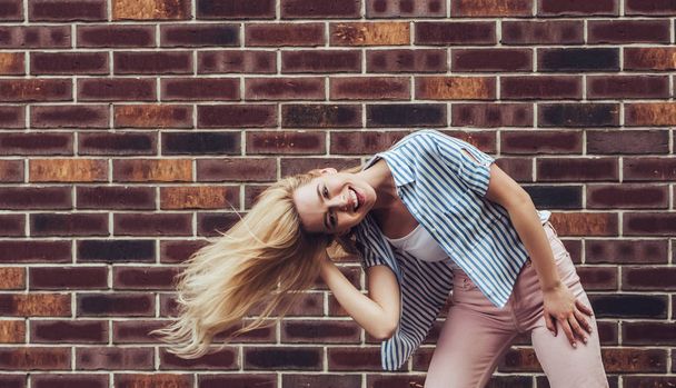 Attractive young woman is posing on brick background in the city. Stylish girl is having fun outdoor. - Fotografie, Obrázek