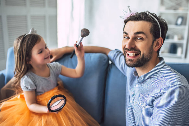 I love you, dad! Handsome young man at home with his little cute girl. Daughter is doing makeup for her daddy. Happy Father's Day! - Foto, afbeelding