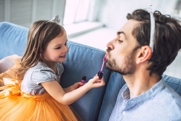 I love you, dad! Handsome young man at home with his little cute girl. Daughter is doing makeup for her daddy. Happy Father's Day! - 写真・画像