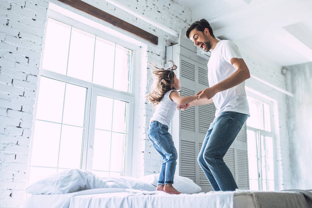 I love you, dad! Handsome young man at home with his little cute girl are having fun and jumping on bed. Happy Father's Day! - Fotoğraf, Görsel