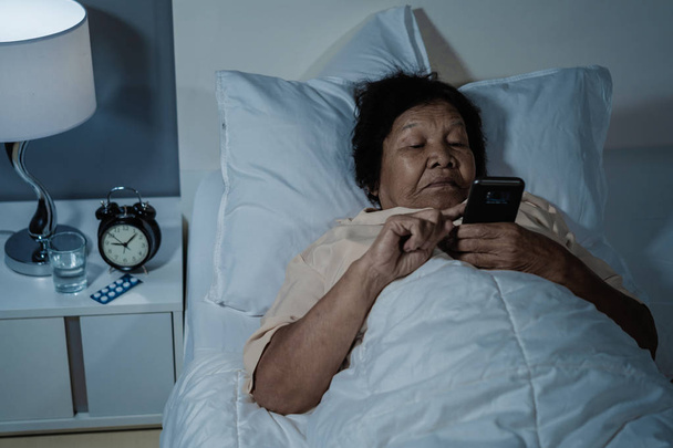 senior woman using mobile phone on a bed at night - Valokuva, kuva