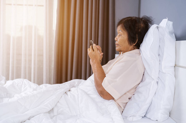 senior woman using mobile phone on a bed - Valokuva, kuva