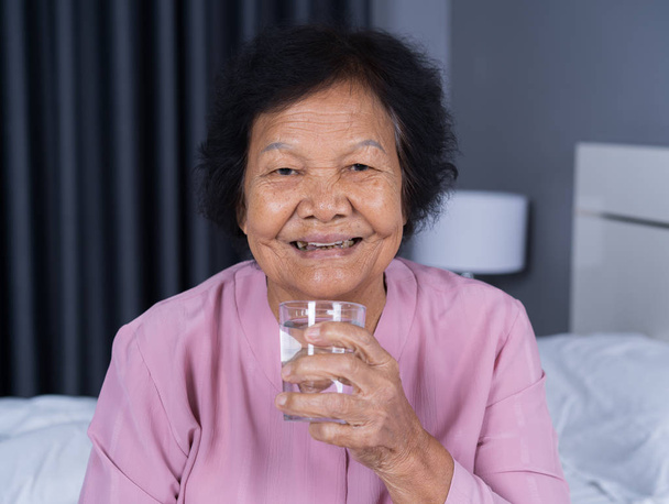 Senior woman drinking water in the bedroom - Foto, afbeelding