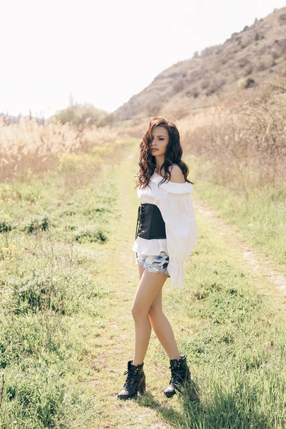 fashion outdoor photo of beautiful woman with dark hair in elegant clothes posing in spring field with reeds - 写真・画像