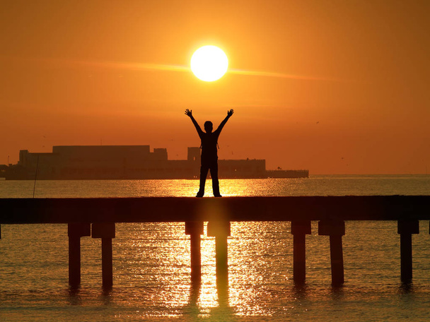 Розумна впевненість чоловік піднімає і відкриває руку під схід сонця на мосту на морі
 - Фото, зображення