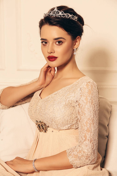 fashion studio photo of beautiful young woman with dark hair and perfect glowing skin, in elegant dress and jewelry diadem, looking like princess  - Фото, изображение
