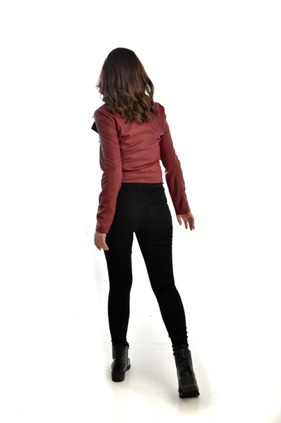 Ολόσωμο πορτρέτο μελαχρινή κοπέλα φορώντας κόκκινο δερμάτινο τζάκετ, μαύρο τζιν και μπότες. όρθια στάση, απομονώνονται σε φόντο λευκό στούντιο. - Φωτογραφία, εικόνα