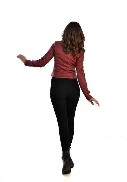 Ganzkörperporträt eines brünetten Mädchens, das rote Lederjacke, schwarze Jeans und Stiefel trägt. Stehende Pose, isoliert auf weißem Studiohintergrund. - Foto, Bild