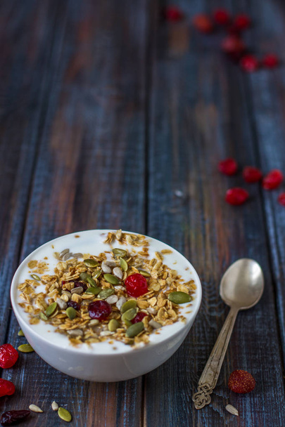 Гранола з йогуртом, сушеними ягодами та гарбузовим насінням на столі з темного дерева
 - Фото, зображення