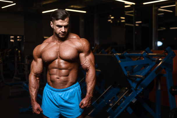 Handsome young fit muscular caucasian man of model appearance workout training in the gym gaining weight pumping up muscle, poses, drinks water  fitness and bodybuilding sport nutrition concept - Fotó, kép
