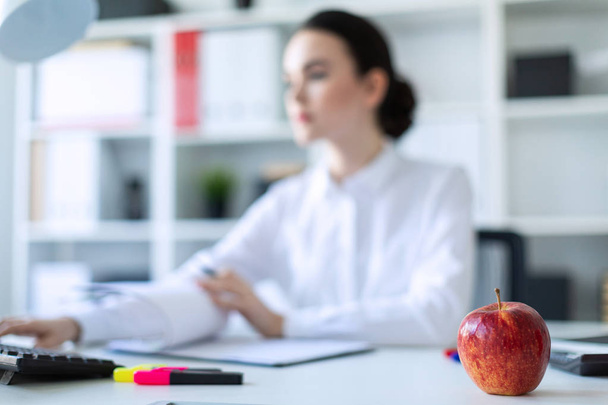 Mladá dívka v kanceláři s jablkem. Fotografie s hloubkou ostrosti, zvýrazněné zaměření na apple. - Fotografie, Obrázek