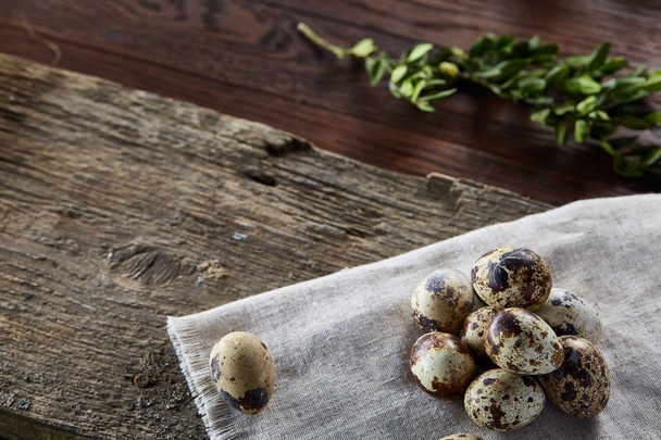 Quail eggs arranged in pyramid on a napkin with boxwood branches over a wooden table, close-up, selective focus. - Φωτογραφία, εικόνα