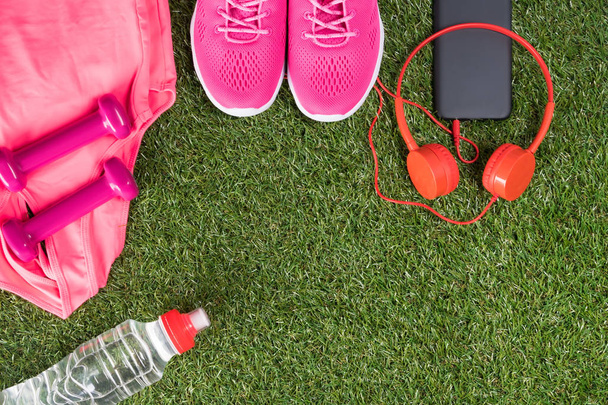 pink set of sports things for fitness with music and a bottle of water on a green lawn - Valokuva, kuva