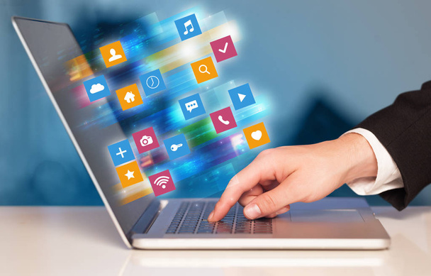 Hand using laptop with colorful application icons and symbols concept - Photo, Image