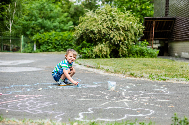 Χαριτωμένο αγόρι και κορίτσι σχέδιο με κιμωλία στο πεζοδρόμιο στο πάρκο. Καλοκαιρινές δραστηριότητες για παιδιά. Δημιουργικό σχέδιο ενός παιδιού με γαλάζια κιμωλία στο δρόμο. - Φωτογραφία, εικόνα
