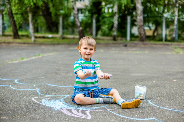 Χαριτωμένο αγόρι και κορίτσι σχέδιο με κιμωλία στο πεζοδρόμιο στο πάρκο. Καλοκαιρινές δραστηριότητες για παιδιά. Δημιουργικό σχέδιο ενός παιδιού με γαλάζια κιμωλία στο δρόμο. - Φωτογραφία, εικόνα