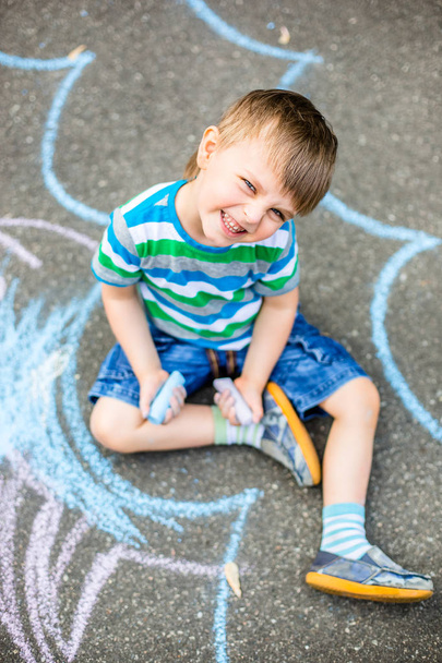 Cute boy and girl drawing with chalk on the sidewalk in the park. Summer activities for children. Creative drawing of a child with blue chalk on the road. - Foto, Bild