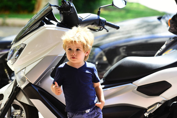 Smart child near the motocycler thumbs up. Good choice. Car and motorcycle shop. A beautiful child and modern transport. Movement and adventure, transport for travel. Dream and future - Φωτογραφία, εικόνα
