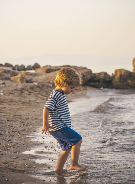 Kind geht am Meer spazieren, Kind spielt mit Wasser am Strand. die Flut im Ozean, ein Sommerspaziergang. Kind und Natur, Küste, Sommer, Tourismus, Urlaub mit Kind. einsamer Junge an der Küste - Foto, Bild