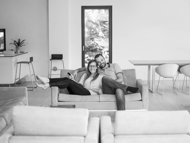 Young couple on the sofa watching television together in their luxury home - Foto, imagen