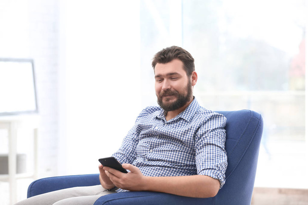 Portrait of confident mature man with mobile phone in armchair - Photo, image