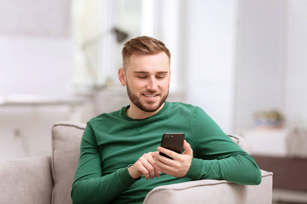 Portrait of confident young man with mobile phone in armchair - Φωτογραφία, εικόνα