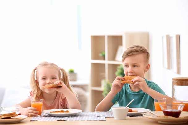 Schattige kleine kinderen lekker geroosterd brood met jam eten aan tafel - Foto, afbeelding