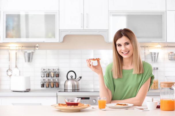 Beautiful woman eating tasty toasted bread with jam in kitchen - Foto, immagini