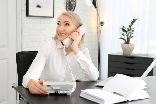 Mature woman talking on phone at workplace - Foto, afbeelding