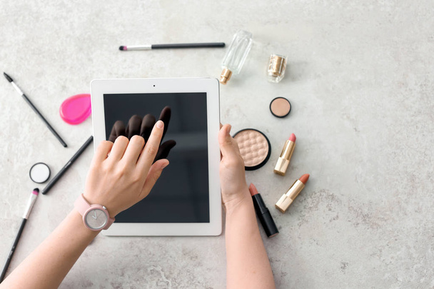 Young woman with makeup products using tablet at table. Beauty blogger - Фото, изображение