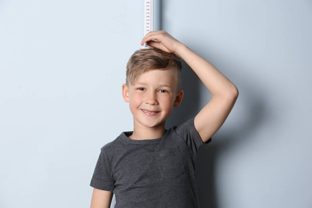Little boy measuring his height on light background - Фото, изображение