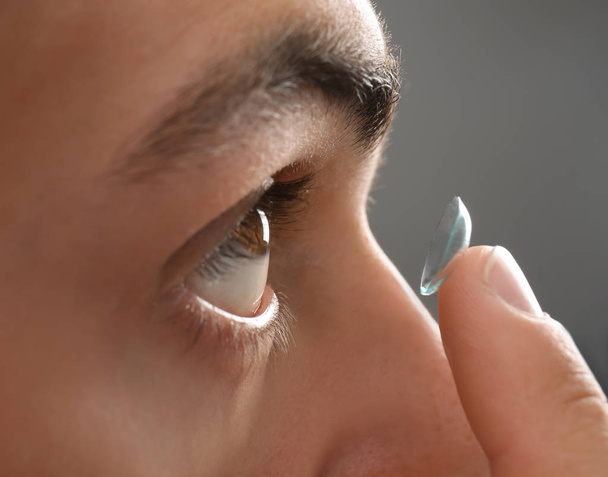 Young man putting contact lens into his eye, closeup - Fotó, kép