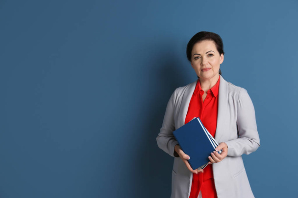 Portrait of female teacher with notebooks on color background - Фото, зображення