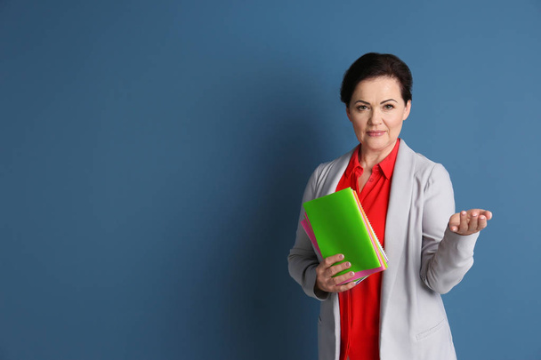 Portrait of female teacher with notebooks on color background - Foto, imagen