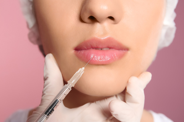 Young woman getting lip injection on color background, closeup - Foto, afbeelding