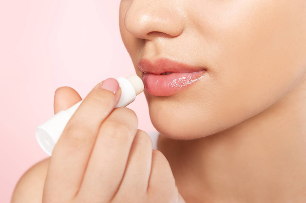 Young woman applying balm on her lips against color background, closeup - Photo, Image