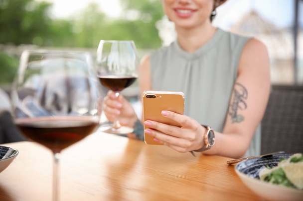 Young woman with smartphone and glass of wine at table - Фото, изображение