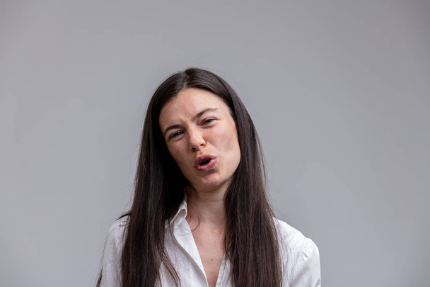 Scornful attractive woman talking to the camera as she jeers at the viewer with a derisory expression and frown over grey with copy space - Photo, Image