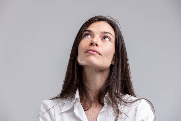 Продумана приваблива жінка, дивлячись в повітря з спокійним споглядальним виразом, ізольована на сірому
 - Фото, зображення