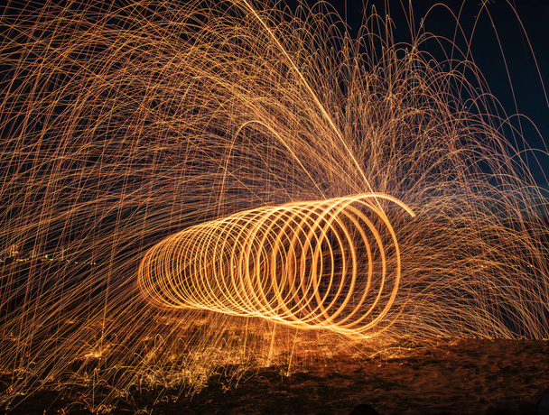 Bola delantera con chispas y llamas larga exposición girando el efecto de la quema de lana de acero en la playa
 - Foto, imagen