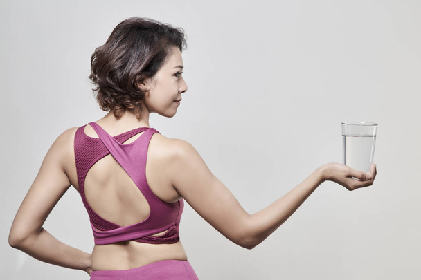 Egy nő visel egy sport ruha lövés után egy pohár vizet, egy szürke háttér, jó egészségügyi koncepció - Fotó, kép