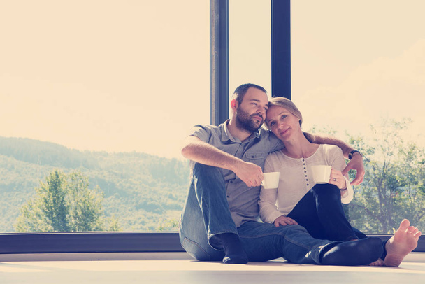 happy romantic couple enjoying morning coffee on the floor by the window in their luxury home - Φωτογραφία, εικόνα